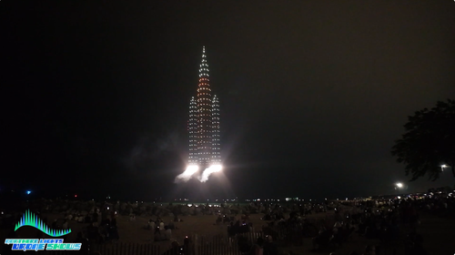 A scene in a drone show depicting drones with fireworks working with regular drones to simulate a spaceship taking off above an audience.